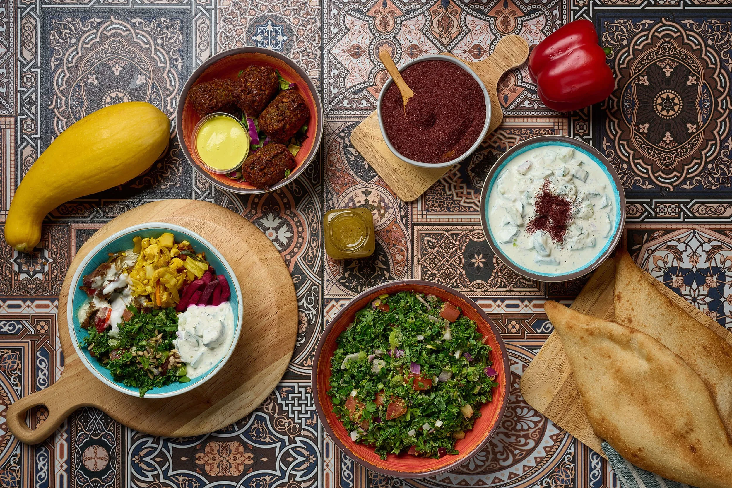 A variety of Middle Eastern dishes on patterned tablecloth, including salad, pita bread, falafel, and assorted sauces.