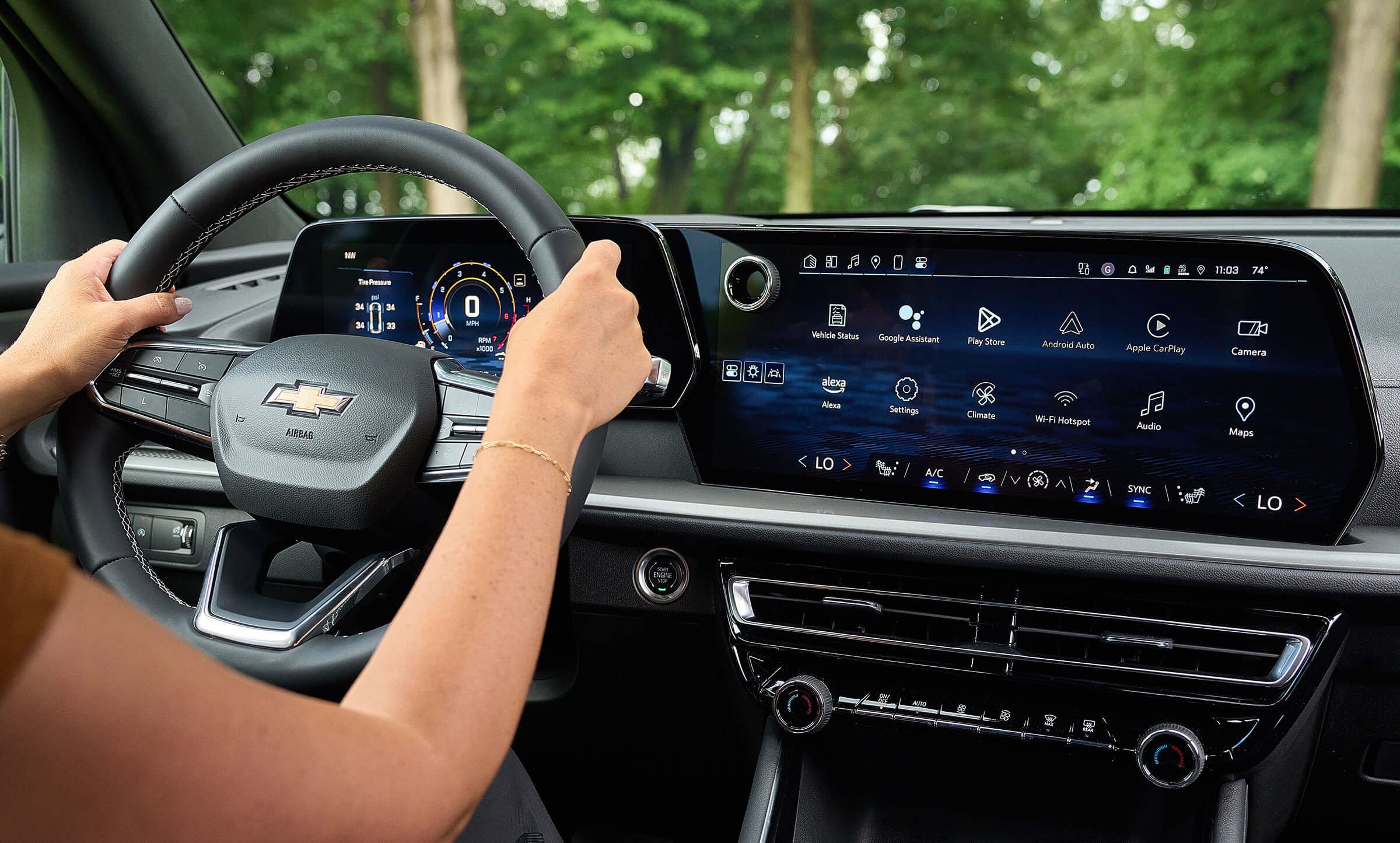 Inside view of a Chevrolet vehicle's dashboard showing a digital instrument cluster and a large touchscreen infotainment system with various app icons, with a person driving in a green outdoor setting.