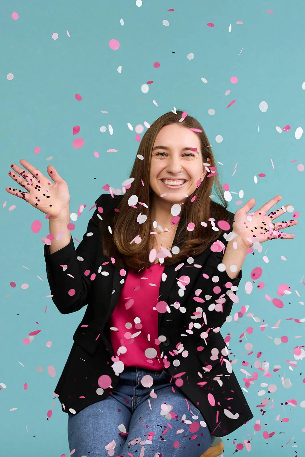 Young woman celebrating with pink and white confetti falling around her, smiling, against a light blue background.