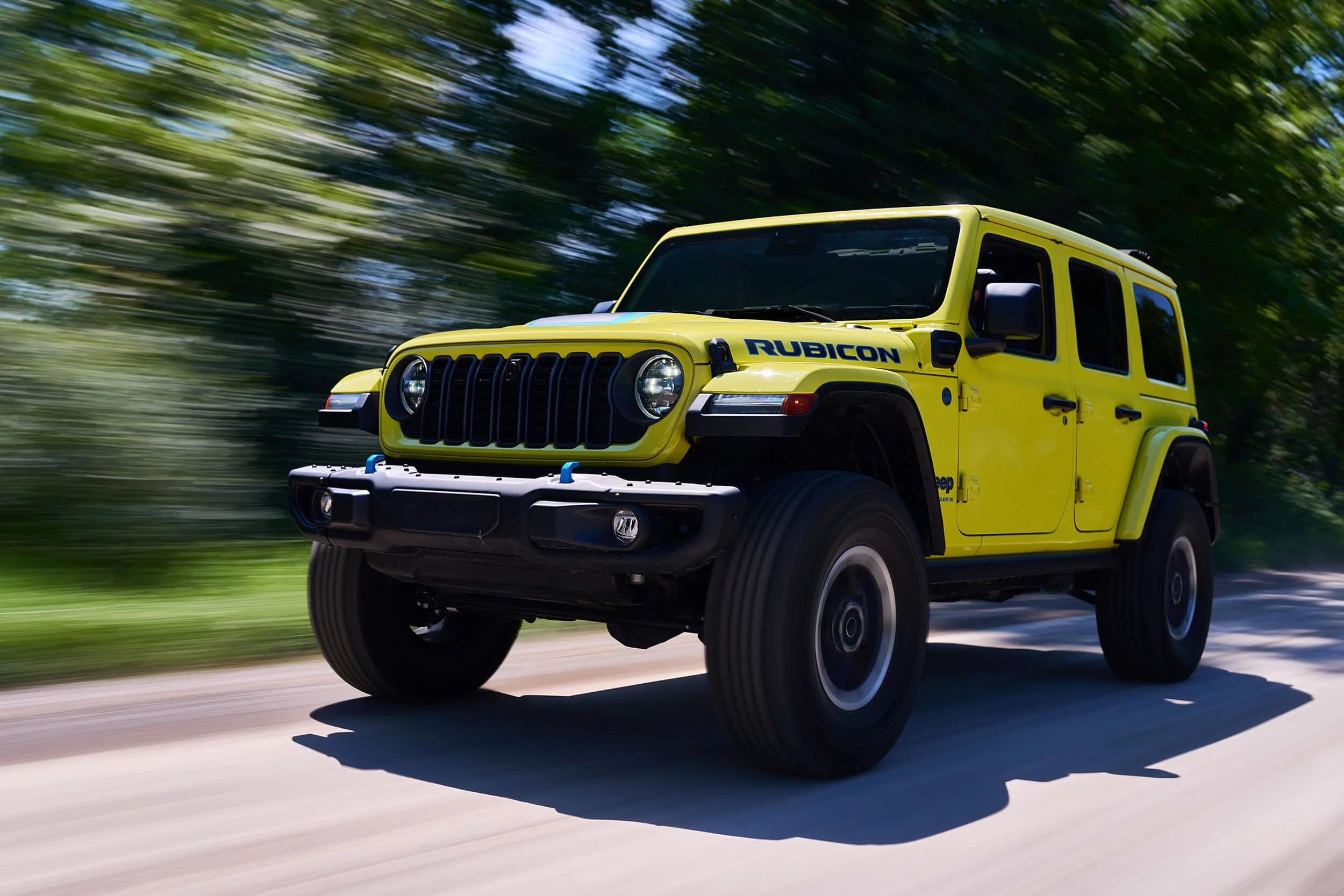 A yellow Jeep Wrangler Rubicon driving on a road with blurred trees in the background.