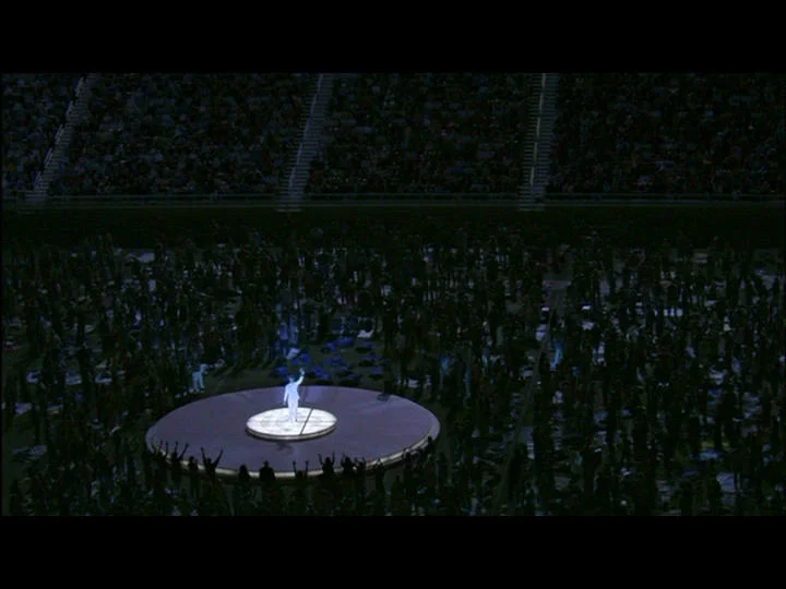 Wide shot of the underlit stage in a stadium full of the faithful.