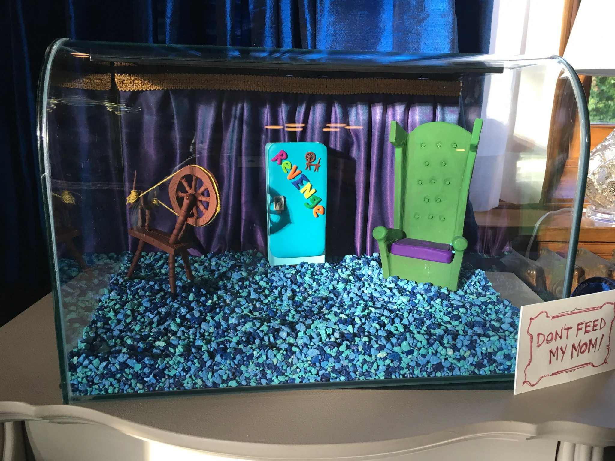 In the first Descendants film Maleficent's raging dragon was reduced to a diminutive lizard by Fairy Godmother (Melanie Paxson). Now that her daughter Mal (Dove Cameron) keeps her in her dorm room, she's tried to make her as comfortable as possible. This lizard cage recalls not only the comforts Maleficent had in the first movie, but gives her back her classic cursed spinning wheel.