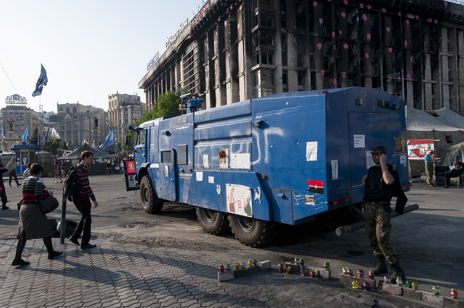A Maidan activist wearing a bulletproof vet next to an immobilized police vehicle 