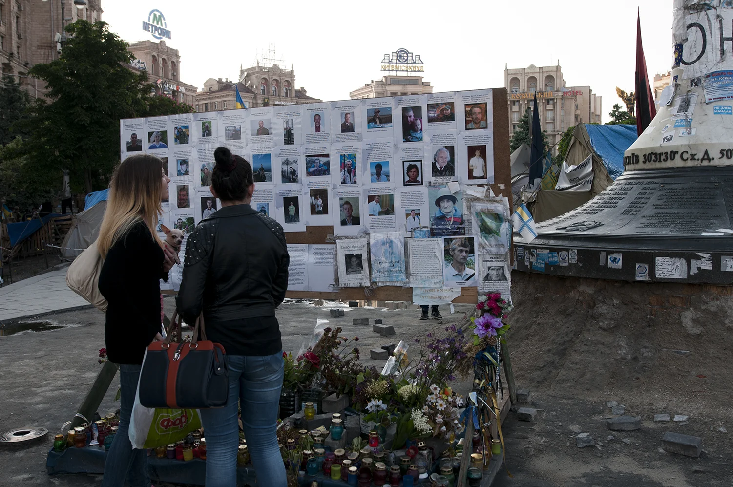 Two young women standing infornt of a board covered with pictures from the Maidan's victimsCar