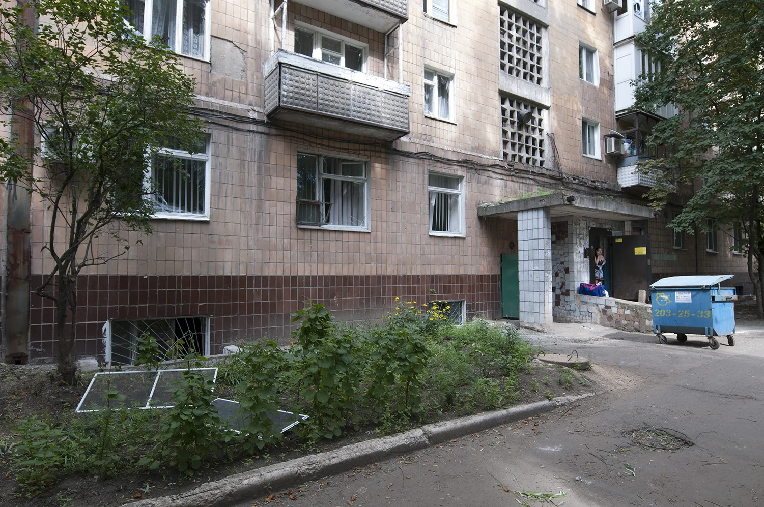 Woman waiting in front of her building with her belonging packed inside bags. All the windows from this site of the building got blown off after a GRAD missile exploded in the middle of this residential area and badly injured a civilian man 