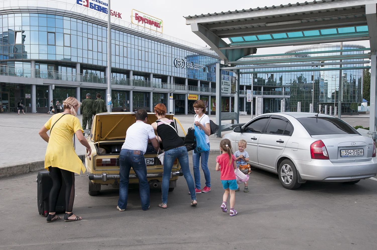 A family rushing to put their suitcases in the trunk of the car before leaving the train station
