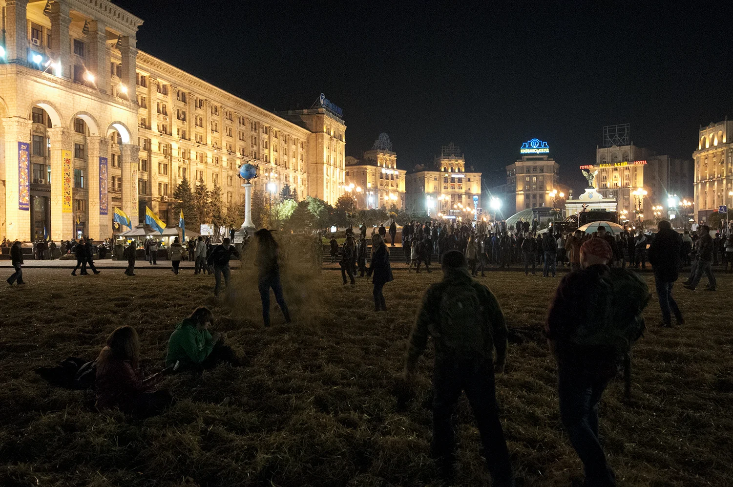 Teens playing in hay as two volunteers walk by on the middle of Maidan Square 