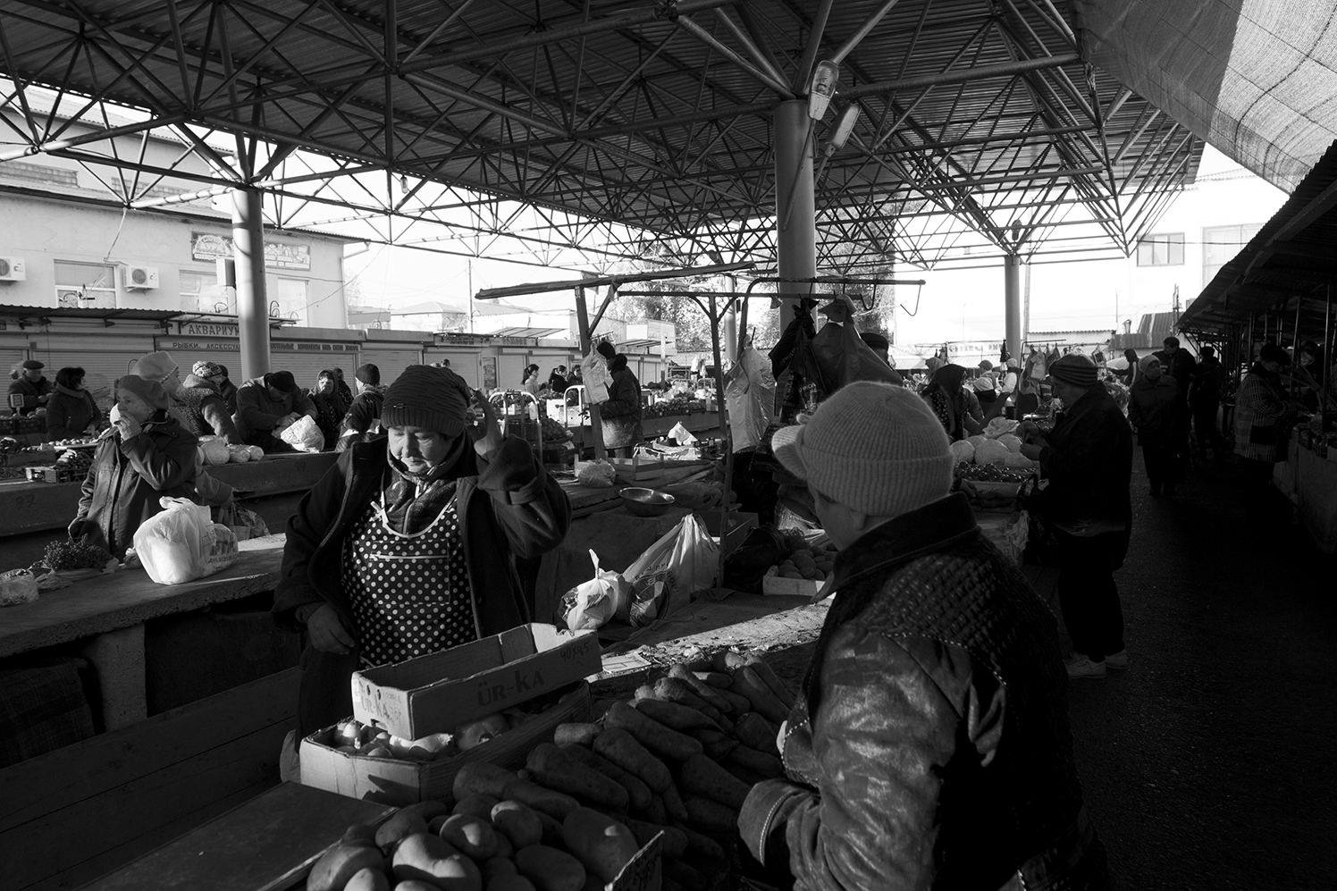 Vender scratching her head as her client look over her carrots and potatoes