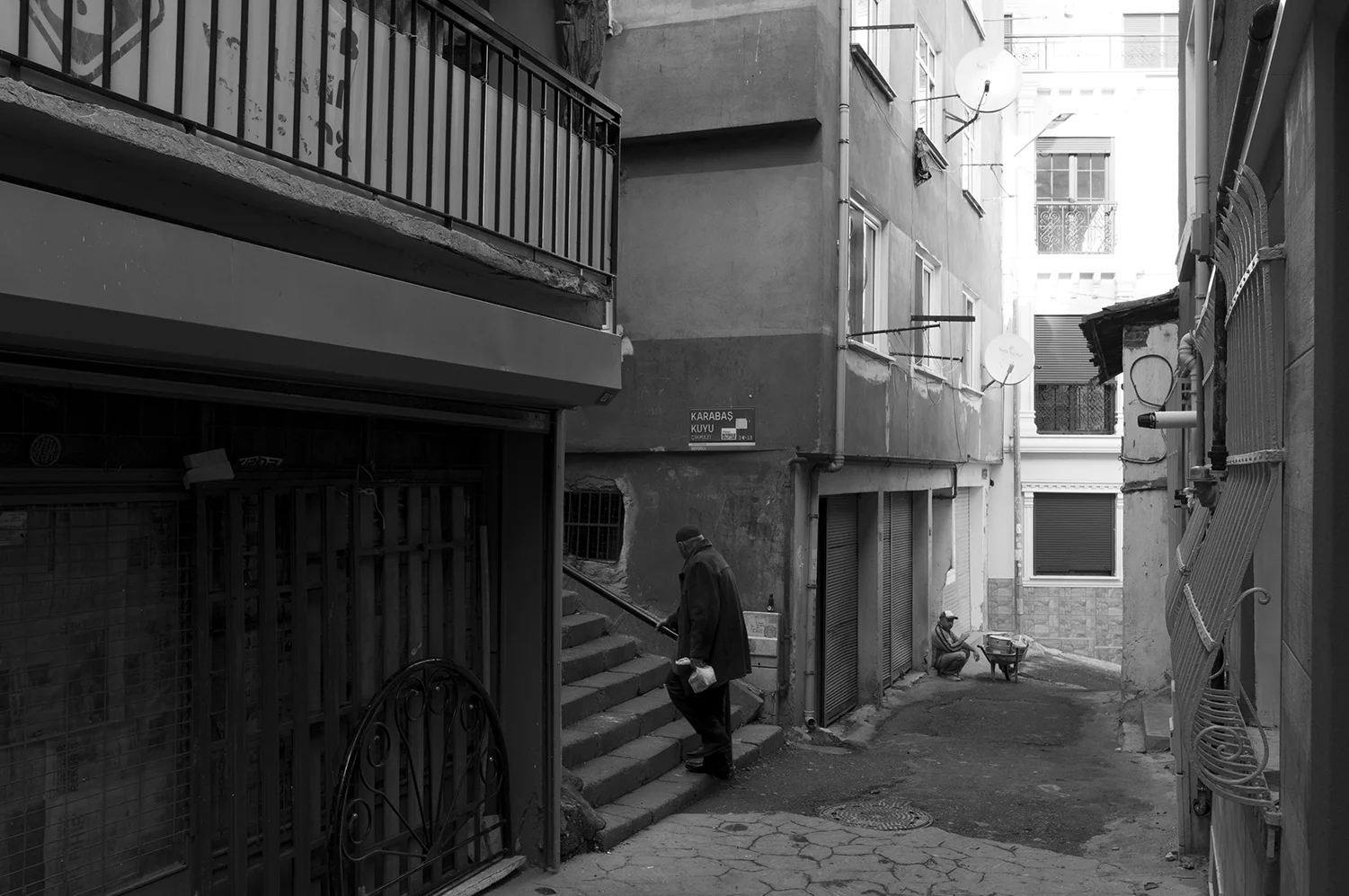 Man walking up to Karabaş Kuyu street as a worker rest next to his wheelbarrow