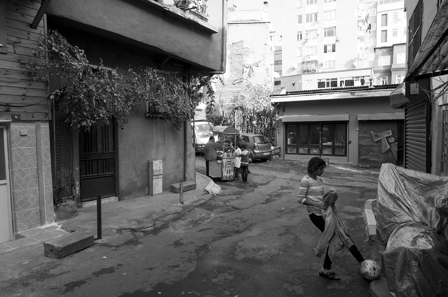 Young girl playing with a football while younger children buy candies from a small kiosk inside Beyoğlu district 