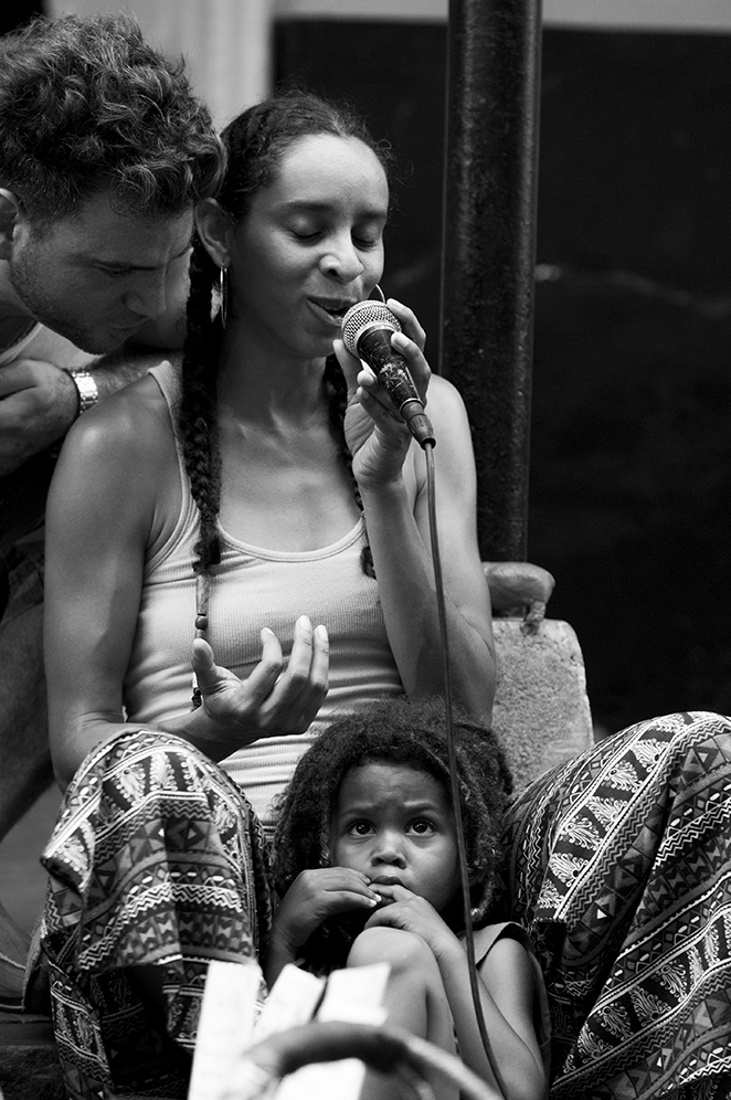 A man whispering in Kelly Love Jones' ear as she sings with her child sitting between her legs.
