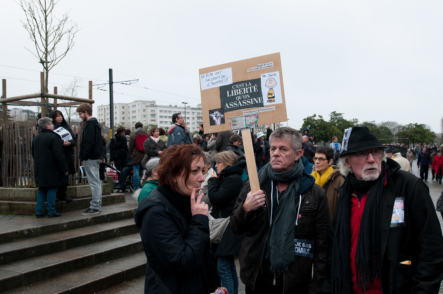 A man holding up a sign saying "The laugh is a Human right" "the joy of life and the revolt of the battle" "It is the liberty that have been murdered"