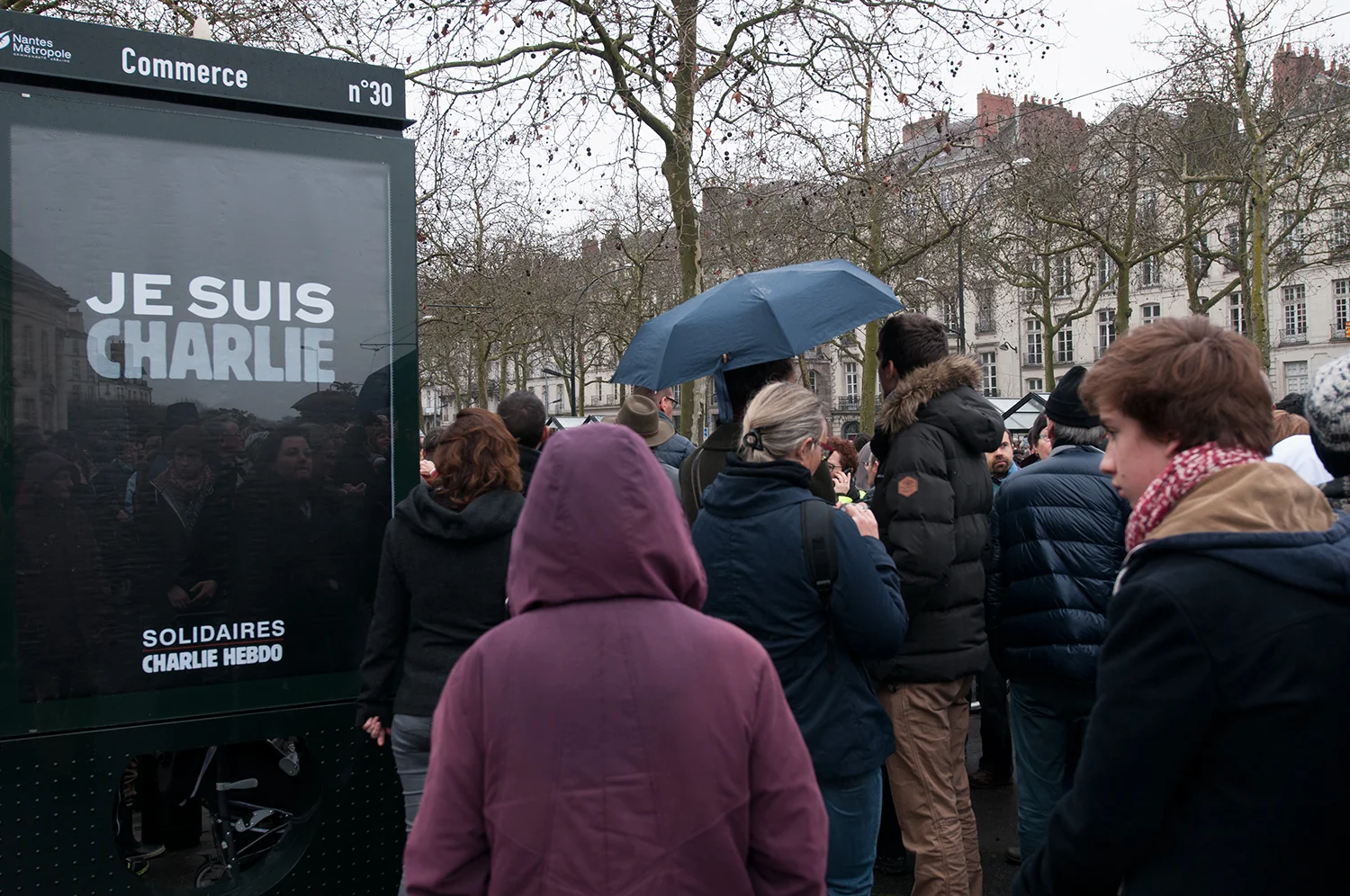 People passing by a poster "I am Charlie, Supporting Charlie Hebdo"