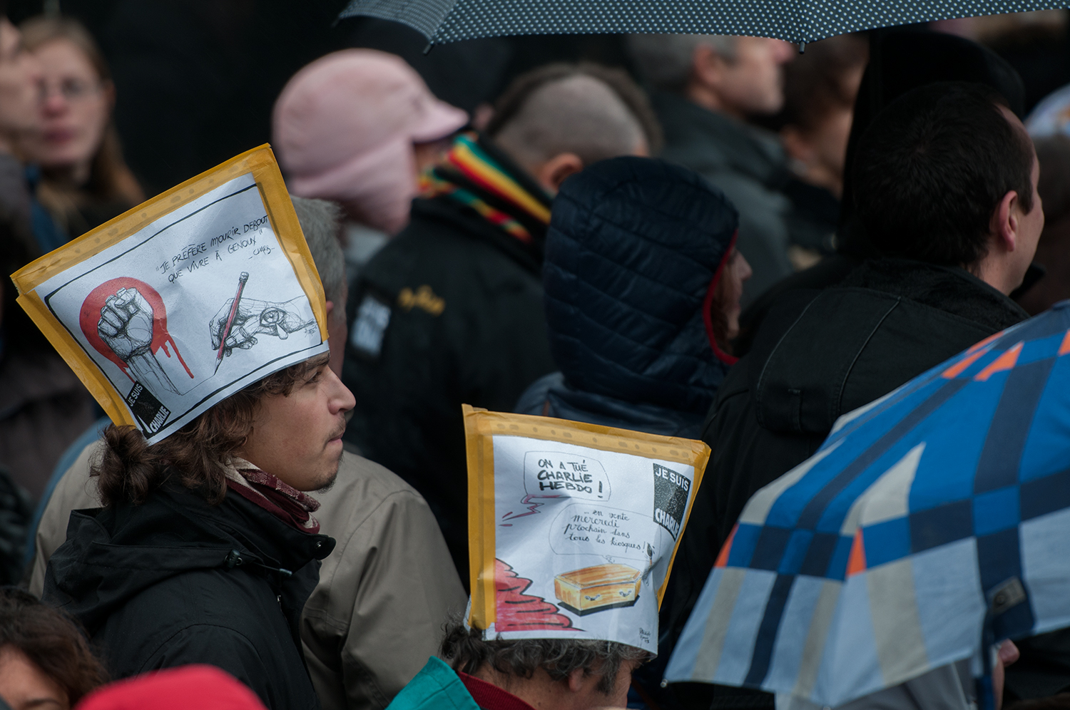 Young man wearing a hat with a quote from Charb saying "I rather die standing than to live on my knees" 