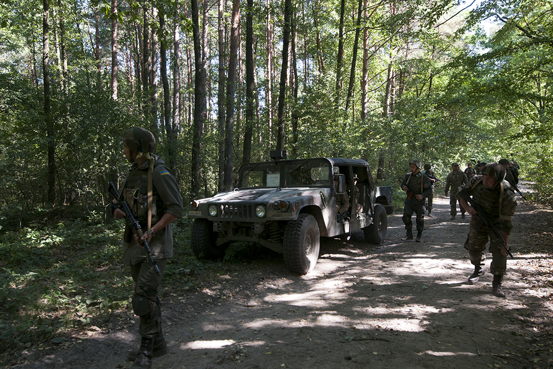 Ukrainian soldiers walking past an American HUMVEE during a patrol exercise.