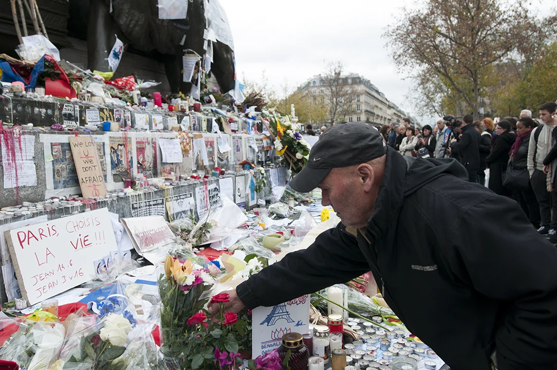 A man adjusting flowers in front of a sign saying "Paris, chose life!!!"