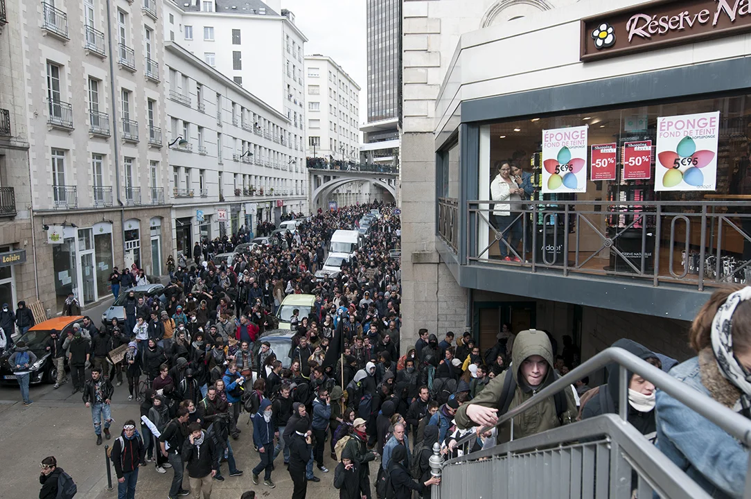 Two women looking from a store window at the protesters climbing stairs in the city center of Nantes.