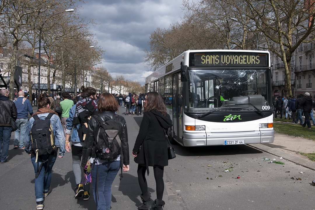 Protersters walking past a vandalized bus.