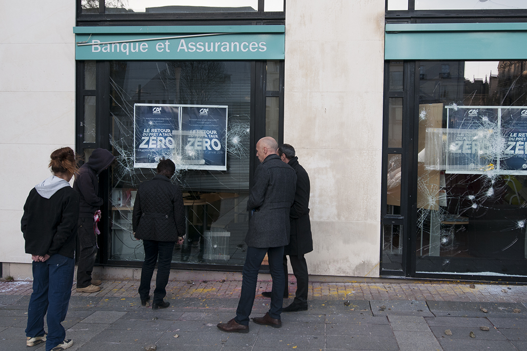 People assessing the damages made by rioters against a bank and insurance agency from the Crédit Agricole.