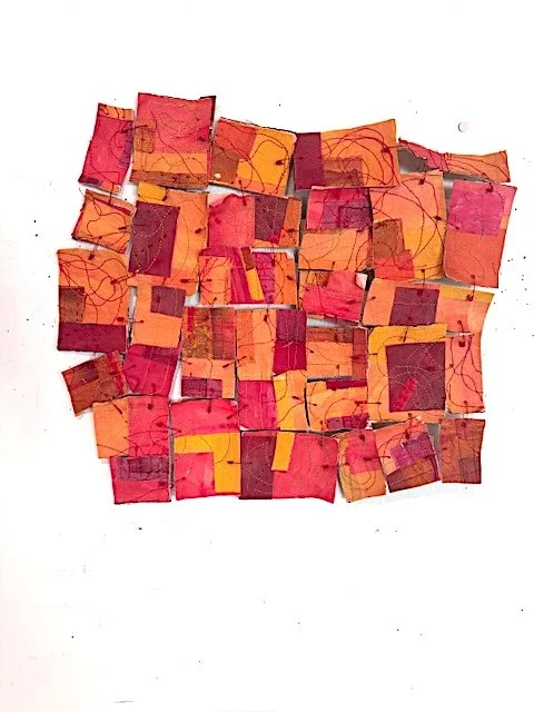 Sculpture of fabric squares in red, orange, and yellow held together with red safety pins