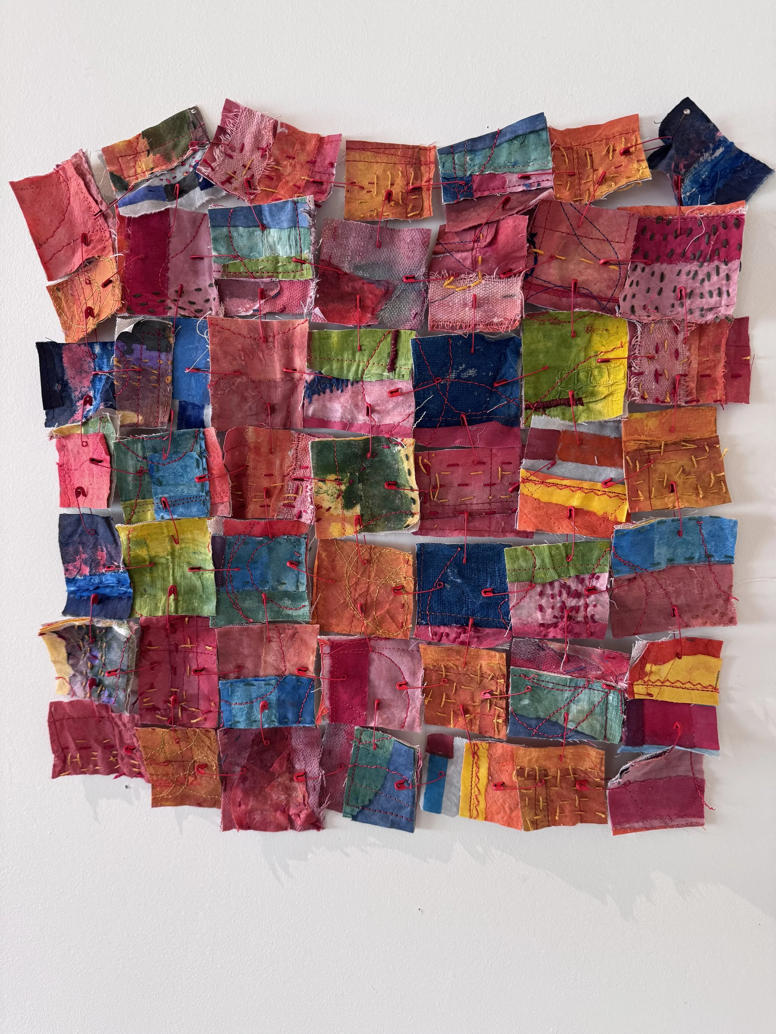 Sculpture of multi-colored fabric squares held together with red safety pins
