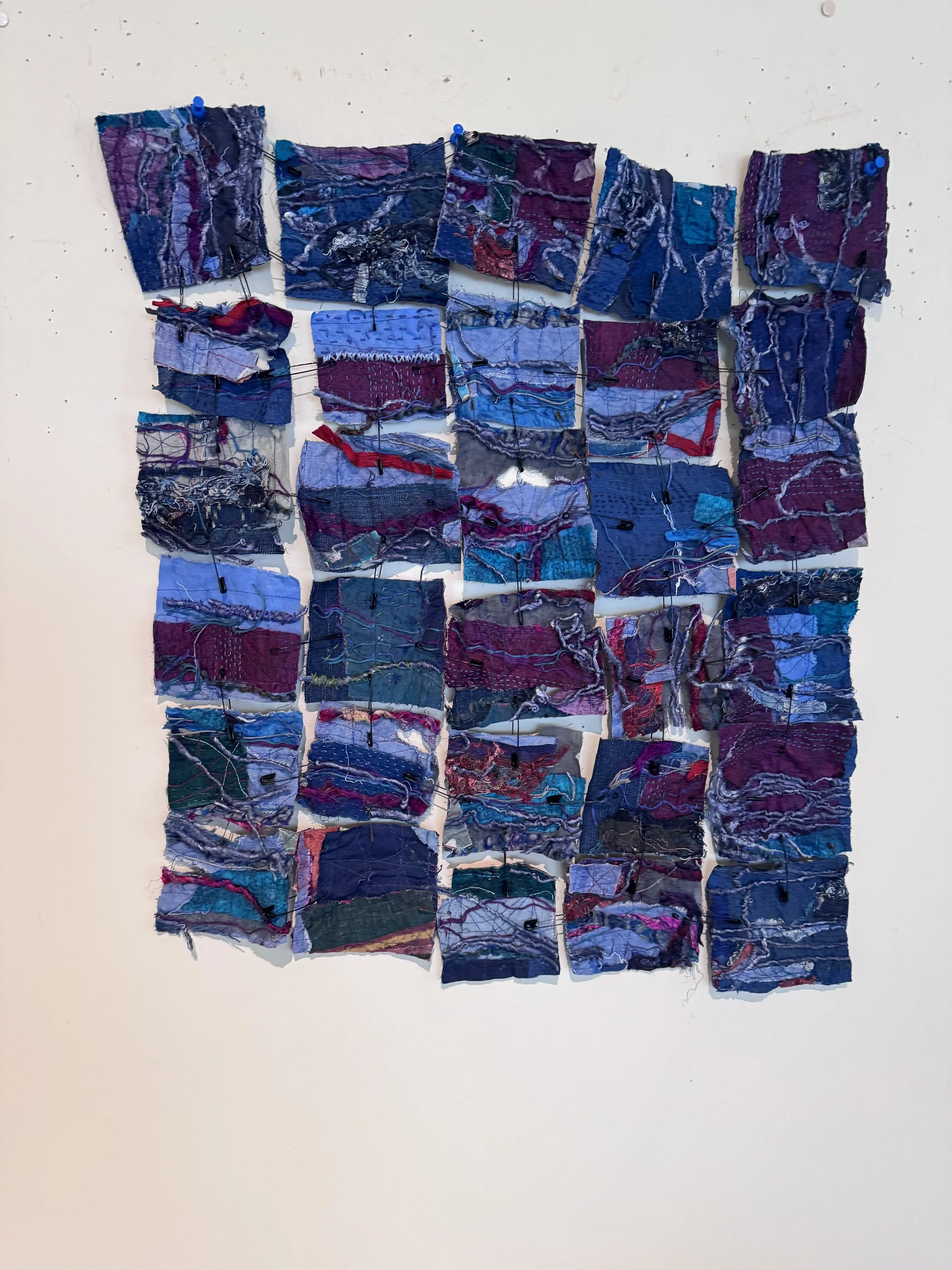 Sculpture of fabric squares in blues and purples held together with blue safety pins