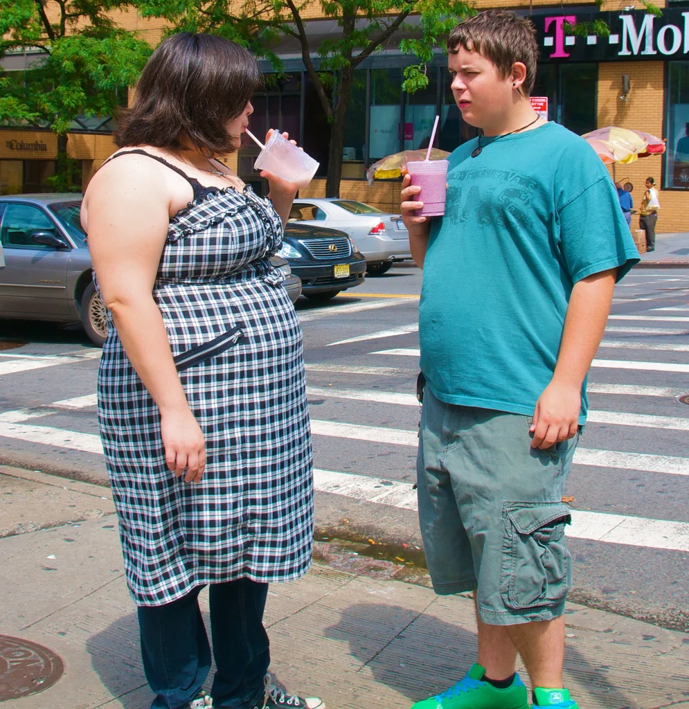 two overweight people drinking smoothies on a street corner