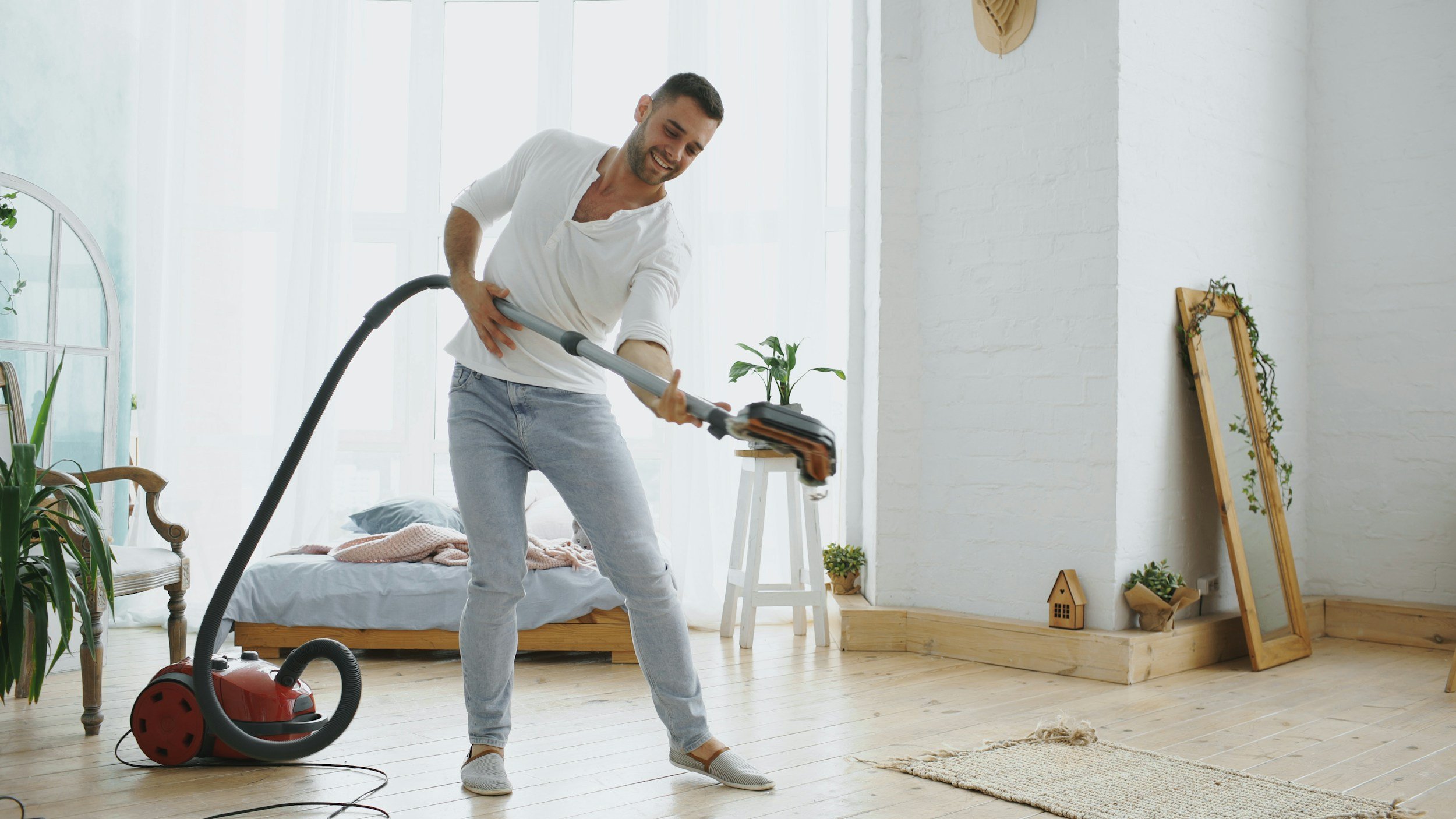 man happily vacuuming room with plants