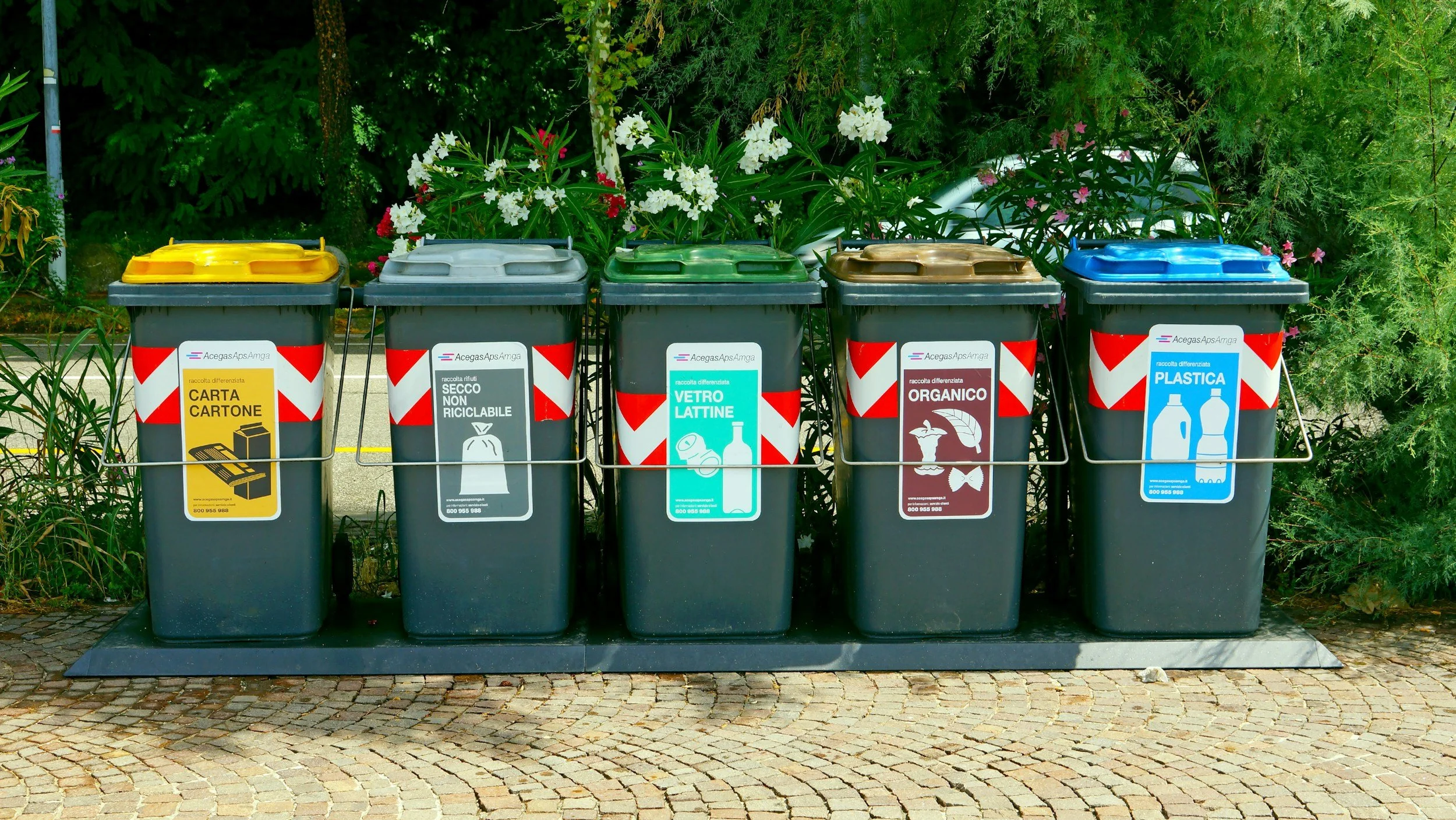 five recycling bins side by side on a sidewalk