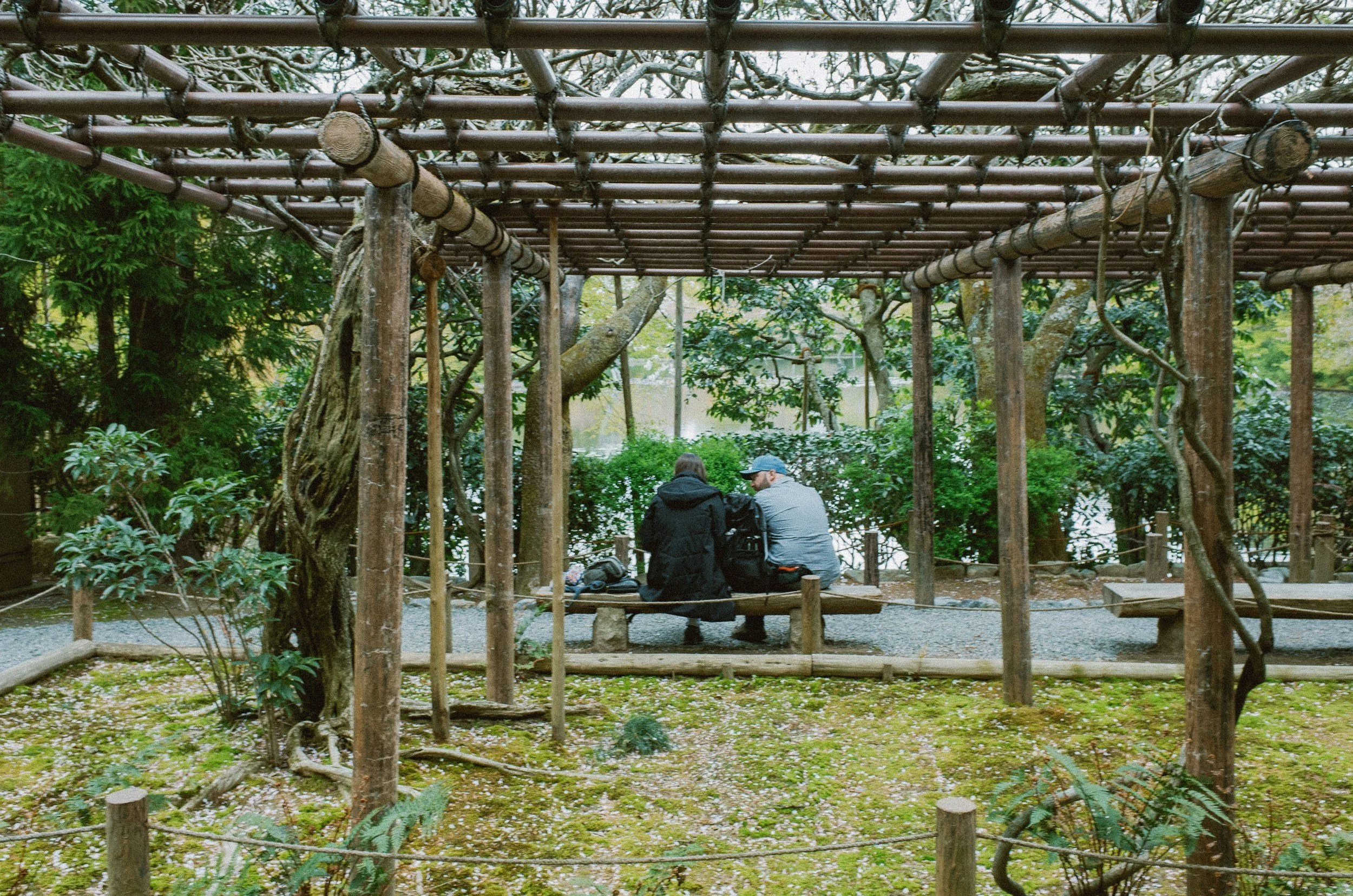 two people sitting on a wooden bench under a pergola