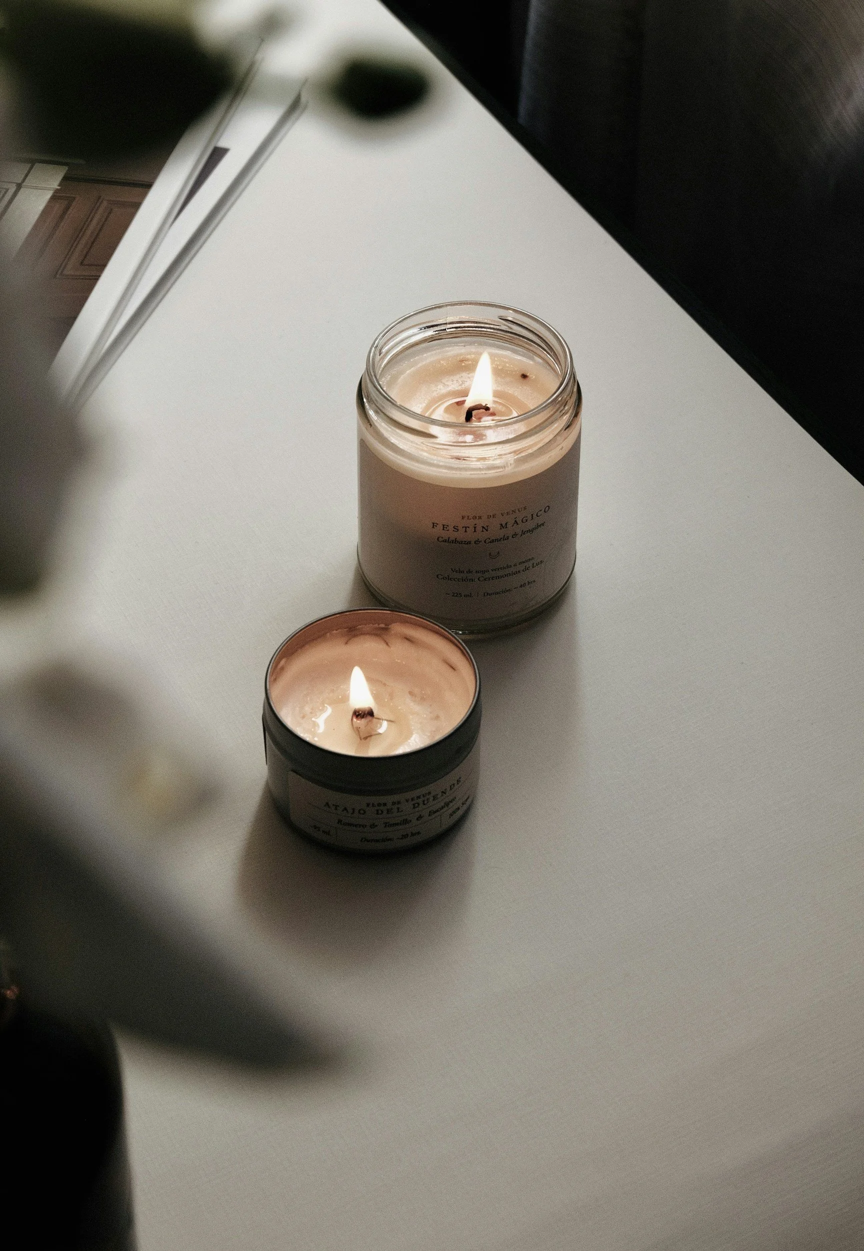 two candles in containers side by side on a white table