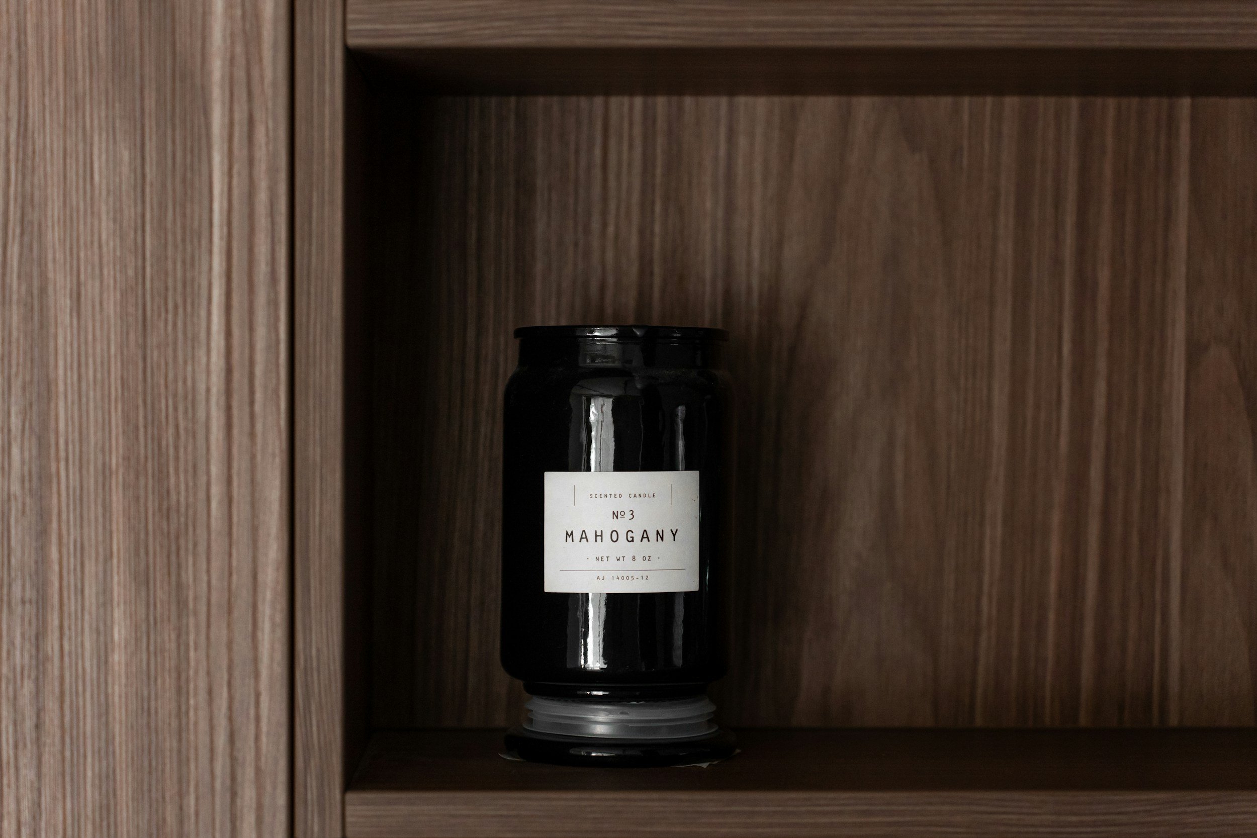 candle in a black jar sitting on a wood shelf
