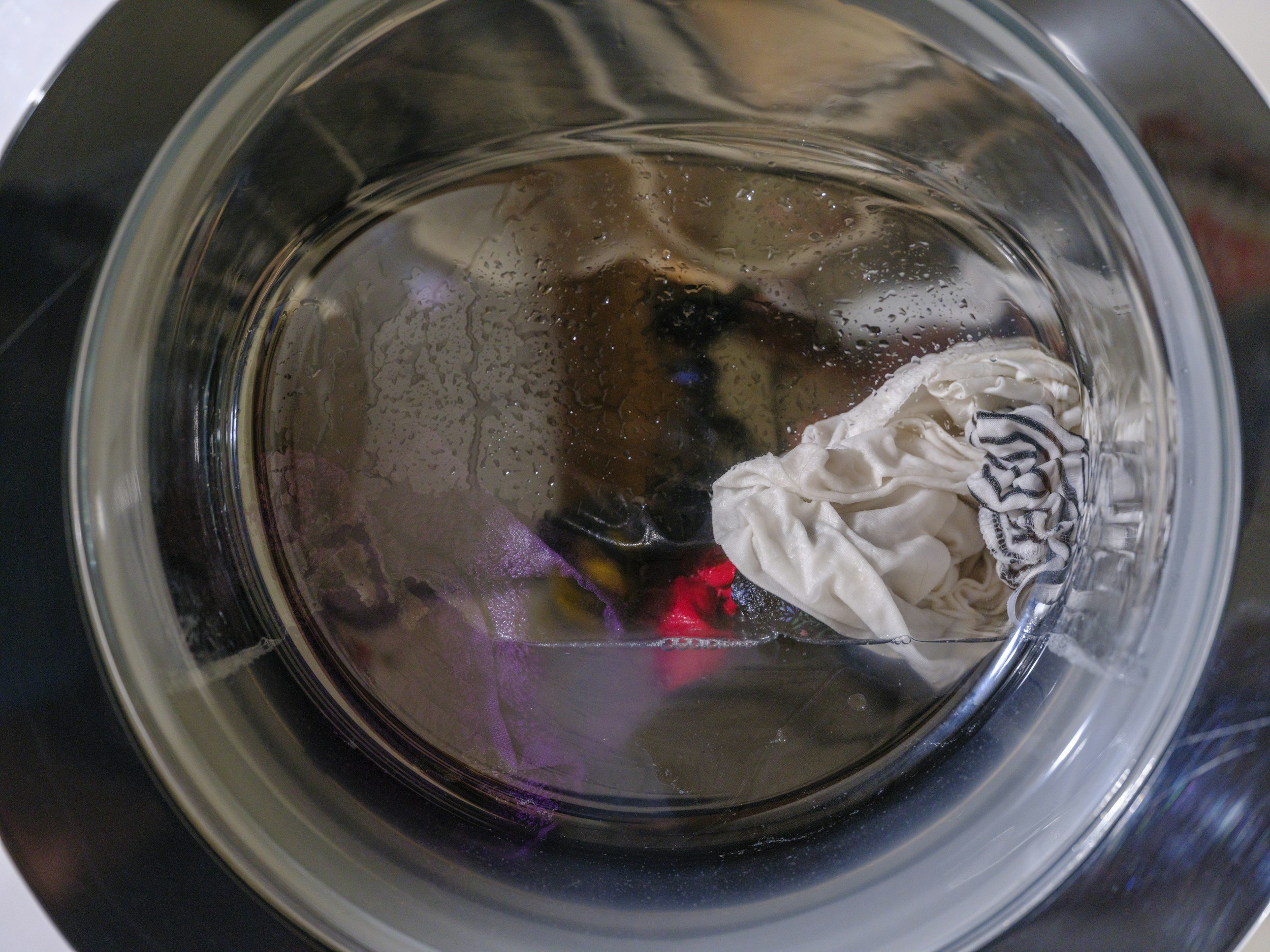 close up of front-loader washing machine with clothes and water