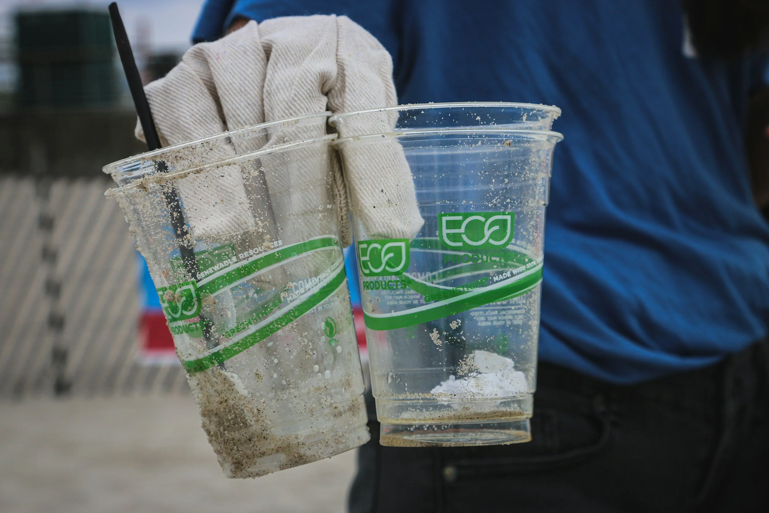person holding two clear plastic disposable cups labeled eco