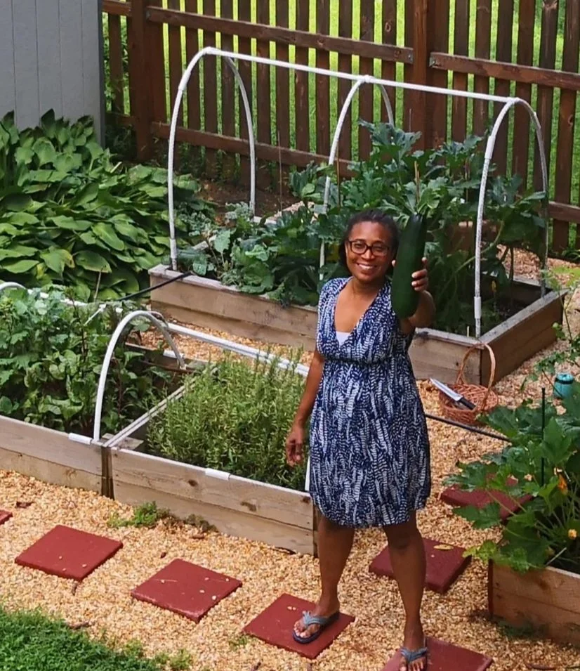 woman standing in front of raised bed garden holding a large zucchini