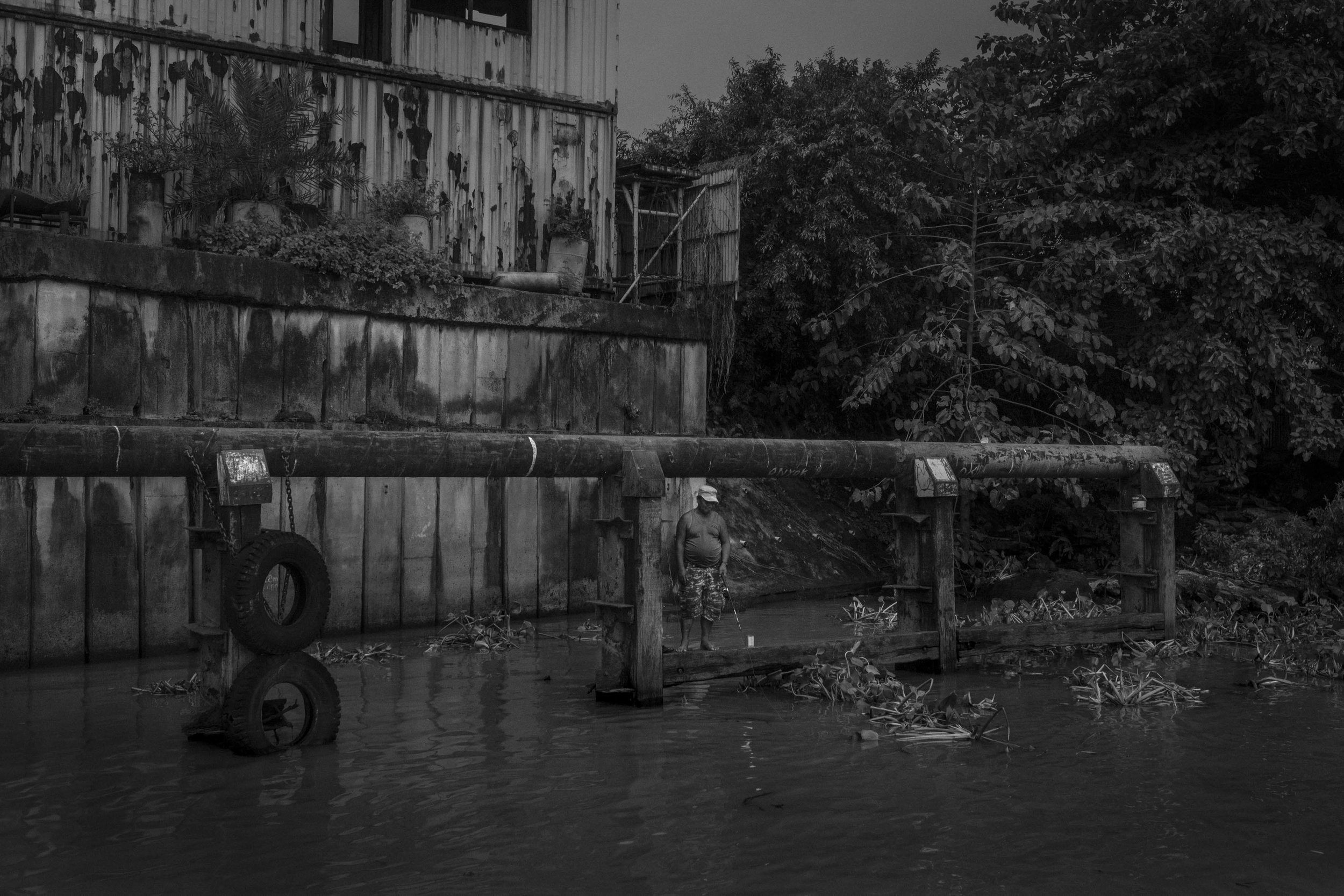  A man fishing next to a disabled industrial building on the banks of Pasig River. 