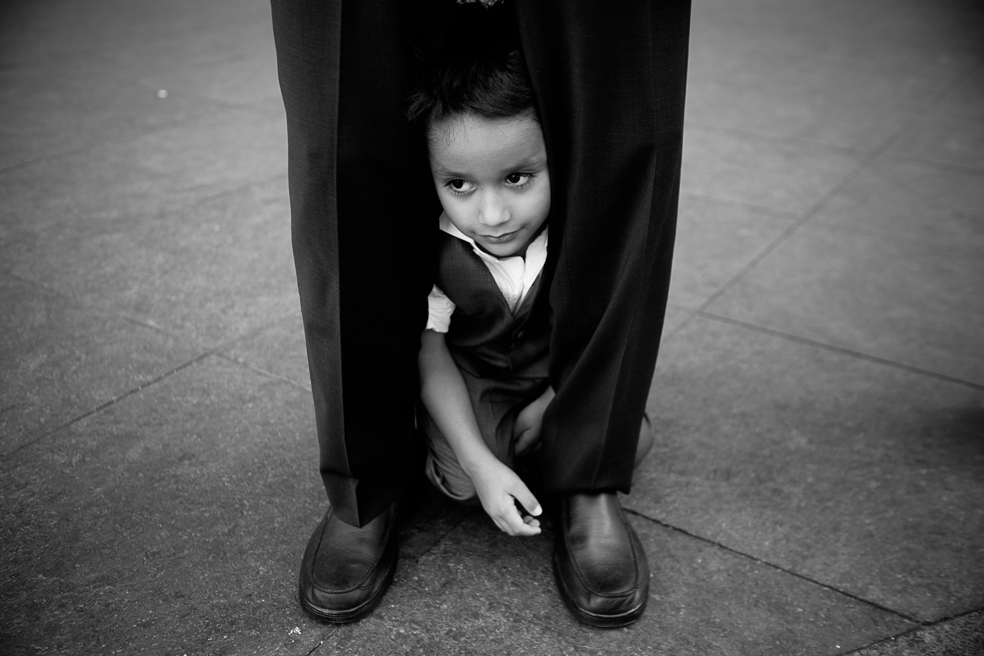  The nephew hides between his dad's legs while waiting to have his portrait taken at the wedding. 