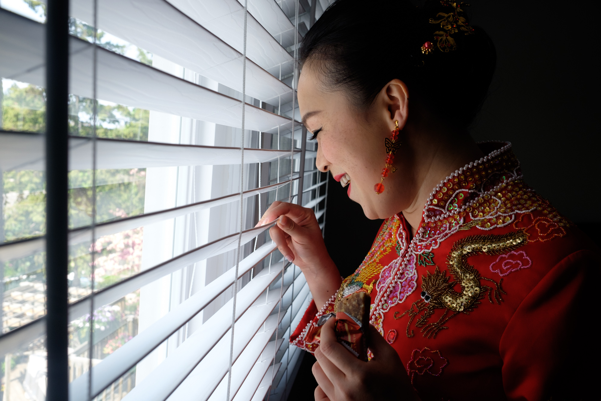  Jing, wearing traditional chinese attire, sneaks a view of guests arriving before her at her wedding ceremony. 