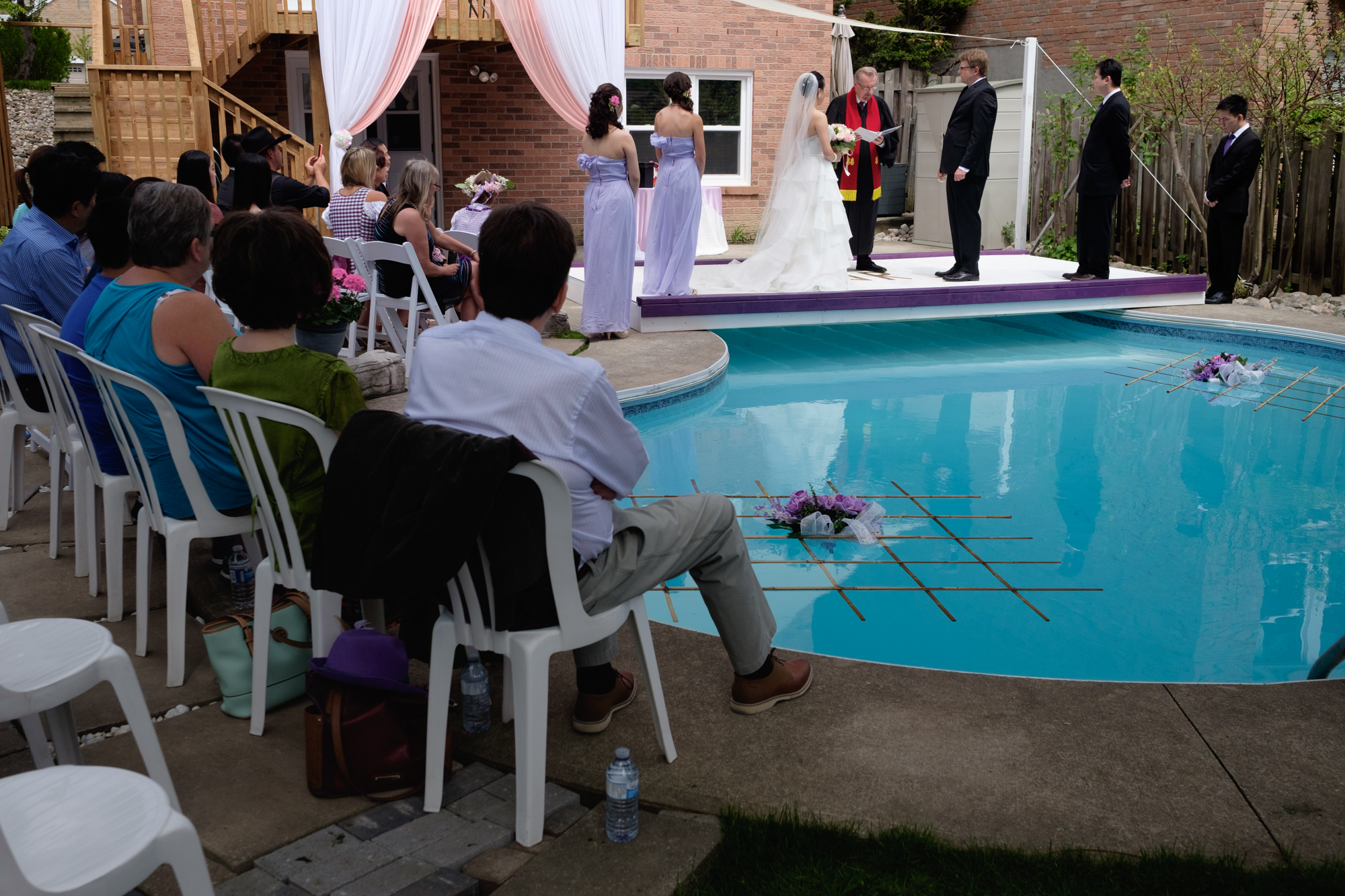  A photograph of Jing + Rene's outdoor wedding ceremony on a platform over their parents backyard pool. 