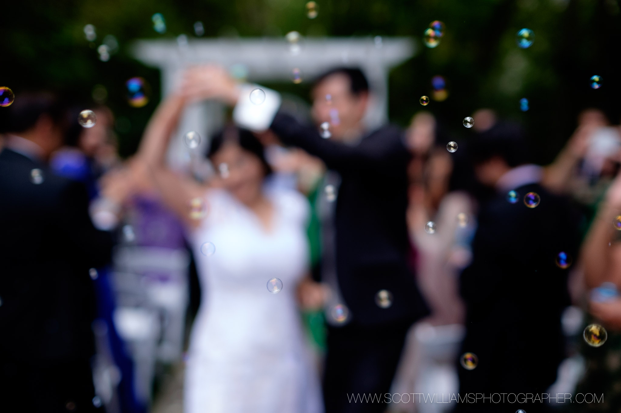 Guests blow bubbles as the bride and groom dance their way up the aisle after their outdoor wedding ceremony at the Ancaster Mill in Ancaster, Ontario. 