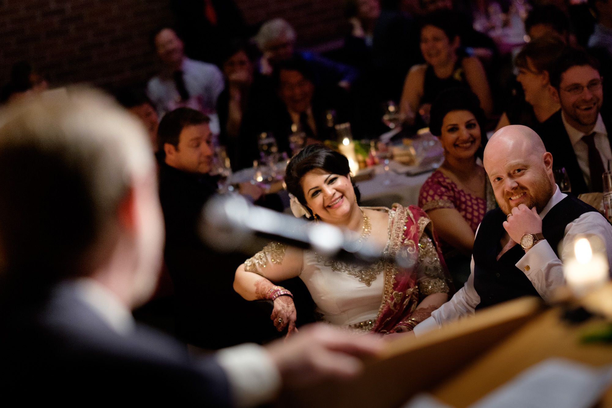 Noor and John look on as the father of the groom gives his wedding toast during their reception at the Toronto Reference Library. 