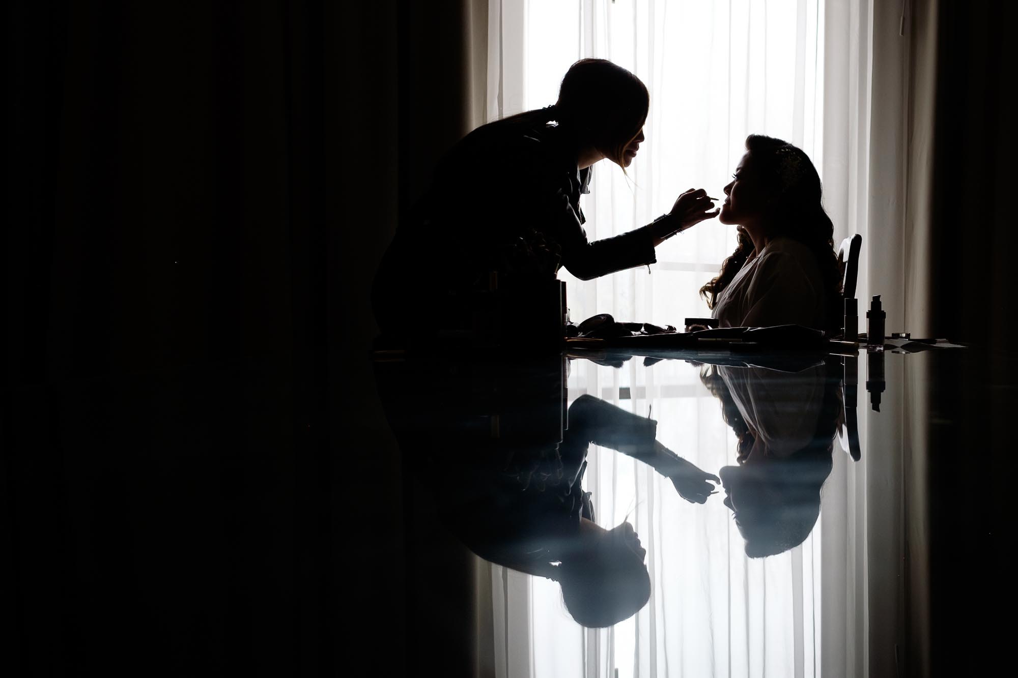  the bride has her makeup applied in her hotel suite before their wedding at the Guild Inn Estate in Toronto, Ontario. 