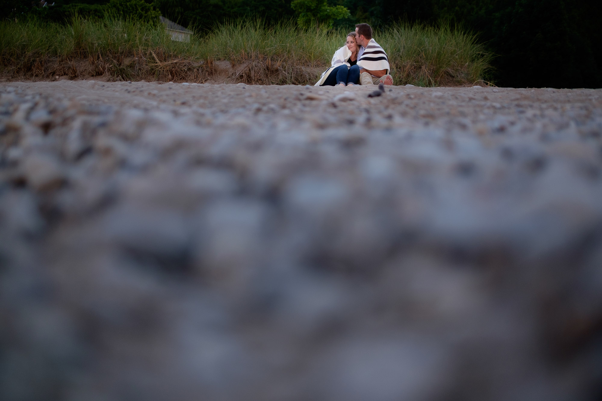  Alex + Colton stay warm under a blanket on a rocky beach during their Goderich engagement shoot. 