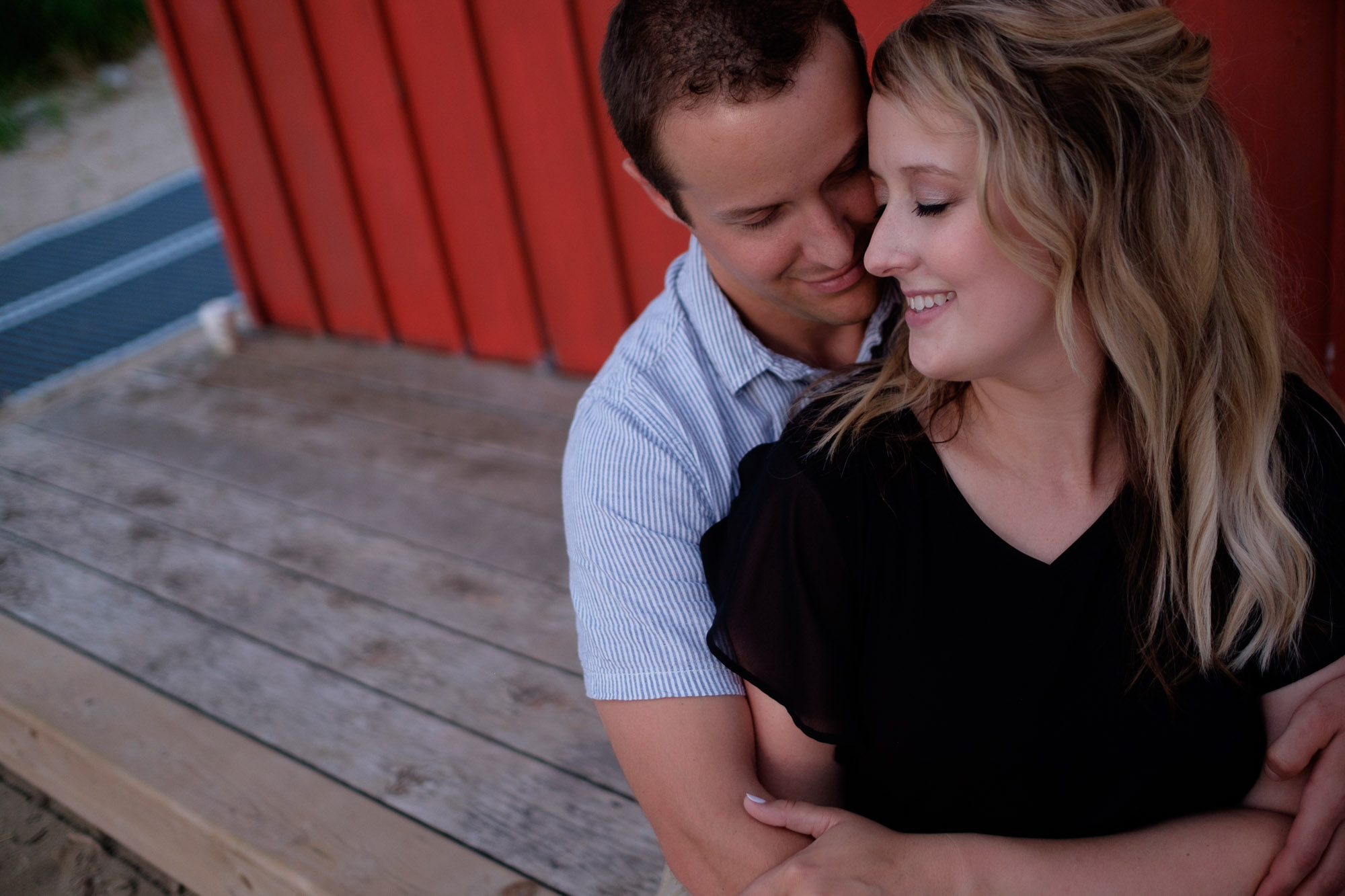 Alex + Colton embrace in front of a beach hut during their waterfront engagement portrait session in Goderich, Ontario on the shores of Lake Huron.