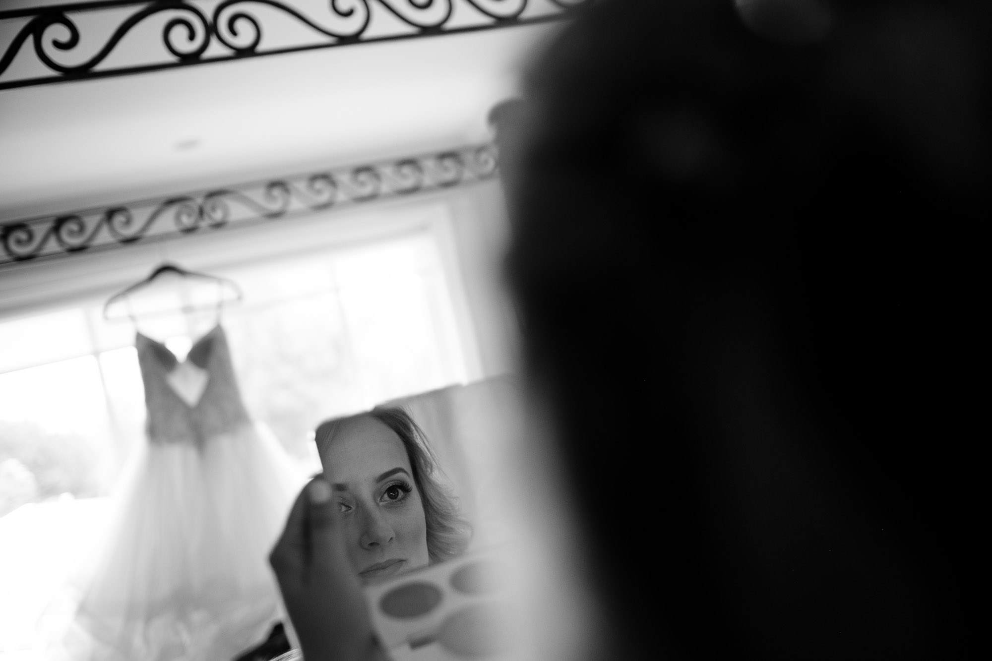  Alex checks her makeup with her wedding dress in the background in this candid black and white wedding photograph. 
