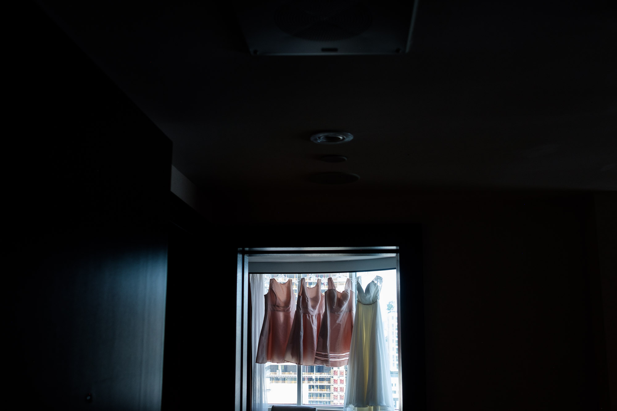 A wedding detail photograph of the brides and bridesmaid dresses hanging up in Katherine’s suite at the Hyatt Toronto.