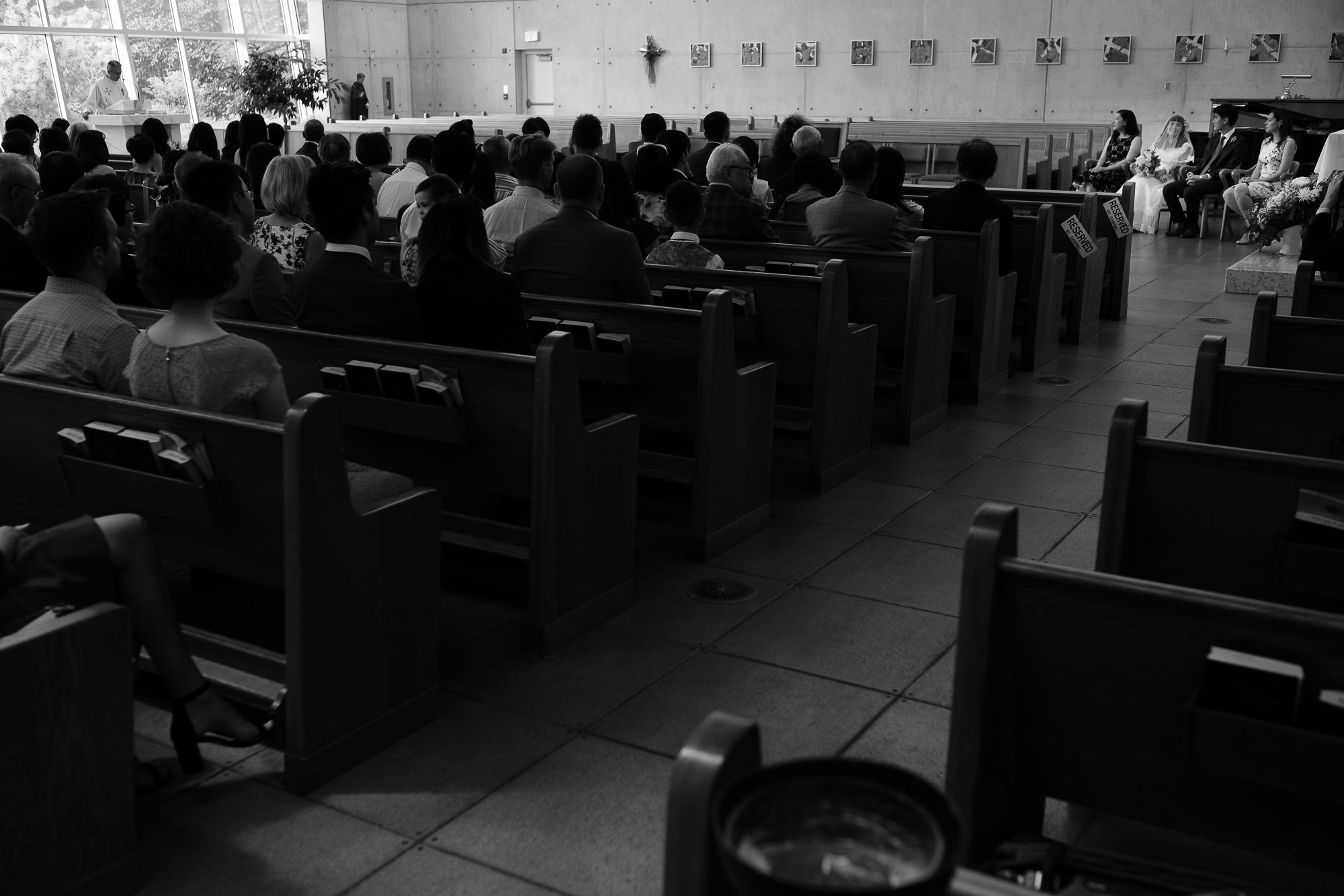 A black and white photograph of the wedding ceremony at St Gabriels Parish church during Huong + Aaron’s catholic wedding ceremony in Toronto.