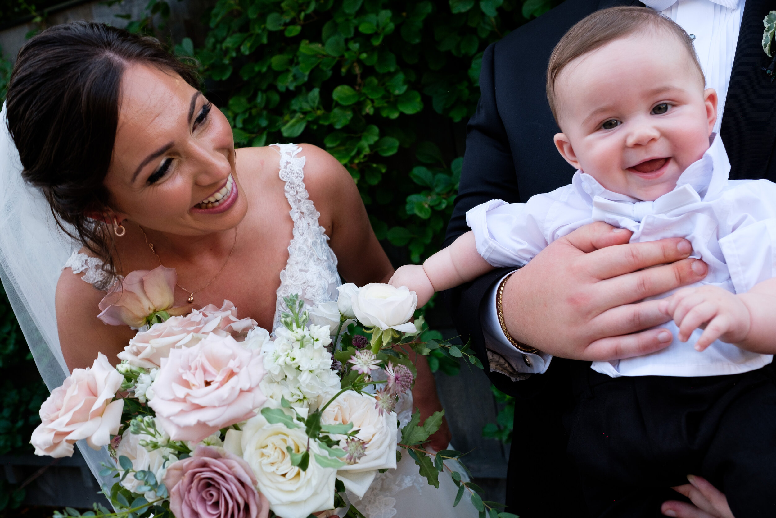  A candid color photograph of the bride and groom interacting with their son during the family portraits at their outdoor wedding at Langdon Hall in Cambridge, Ontario by Toronto wedding photographer Scott Williams (www.scottwilliamsphotogrpaher.com)