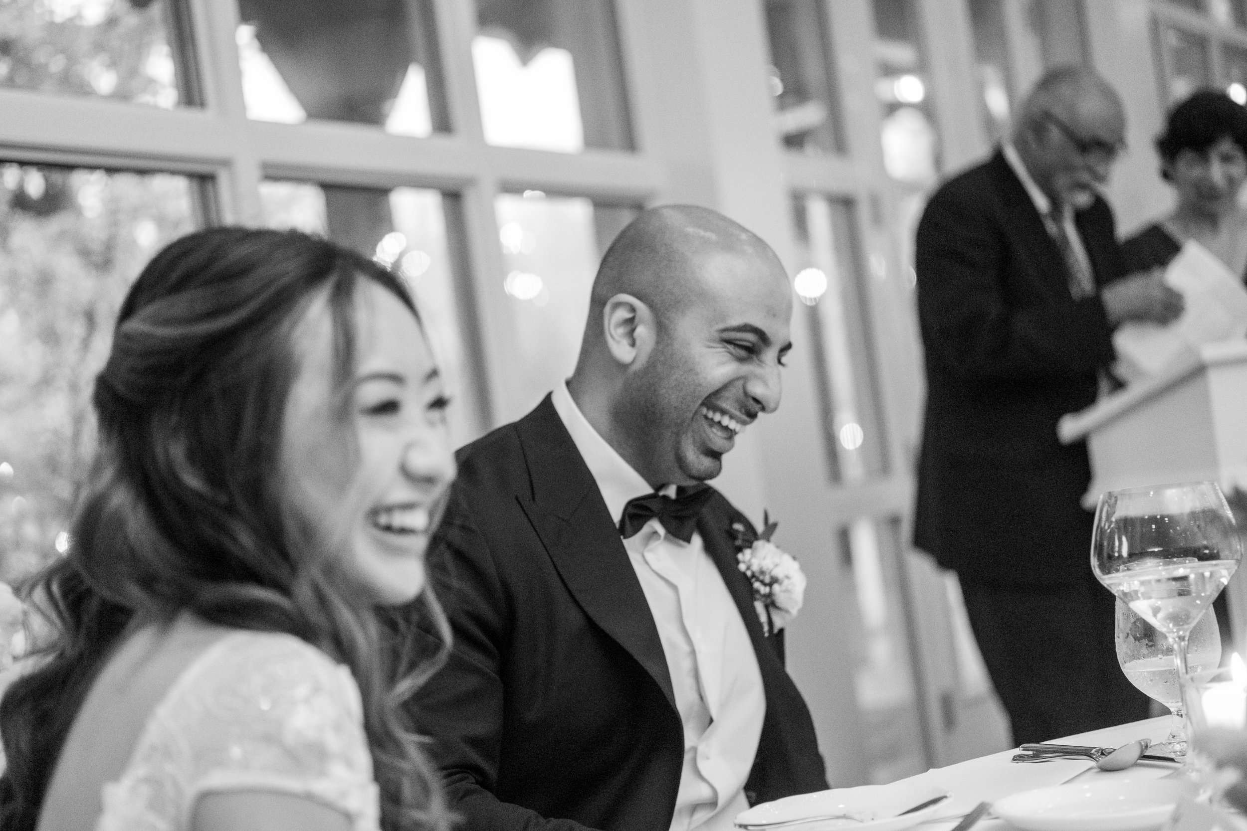  A black and white candid wedding photograph of the wedding couple laughing during a toast during the reception at Tiffany + Zoubin’s wedding at Langdon Hall by Toronto Wedding Photographer Scott Williams  