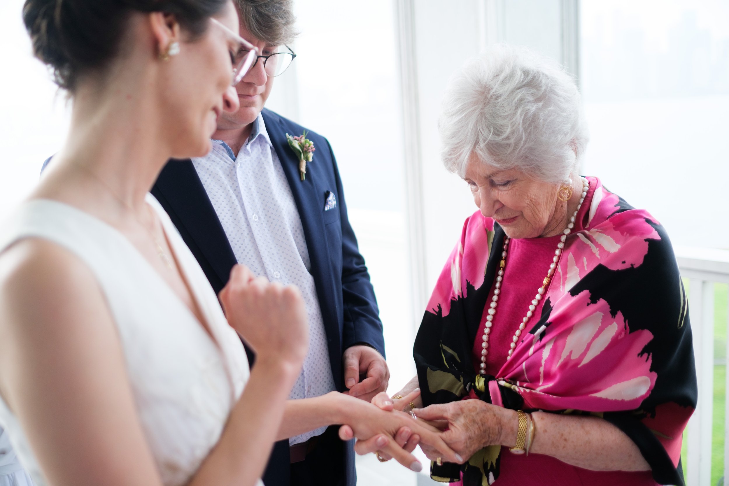  A colour wedding candid photograph of Rocio’s ring being admired by Geoff’s grandmother after their outdoor wedding ceremony at the Royal Canadian Yacht Club by Toronto wedding photographer Scott Williams  